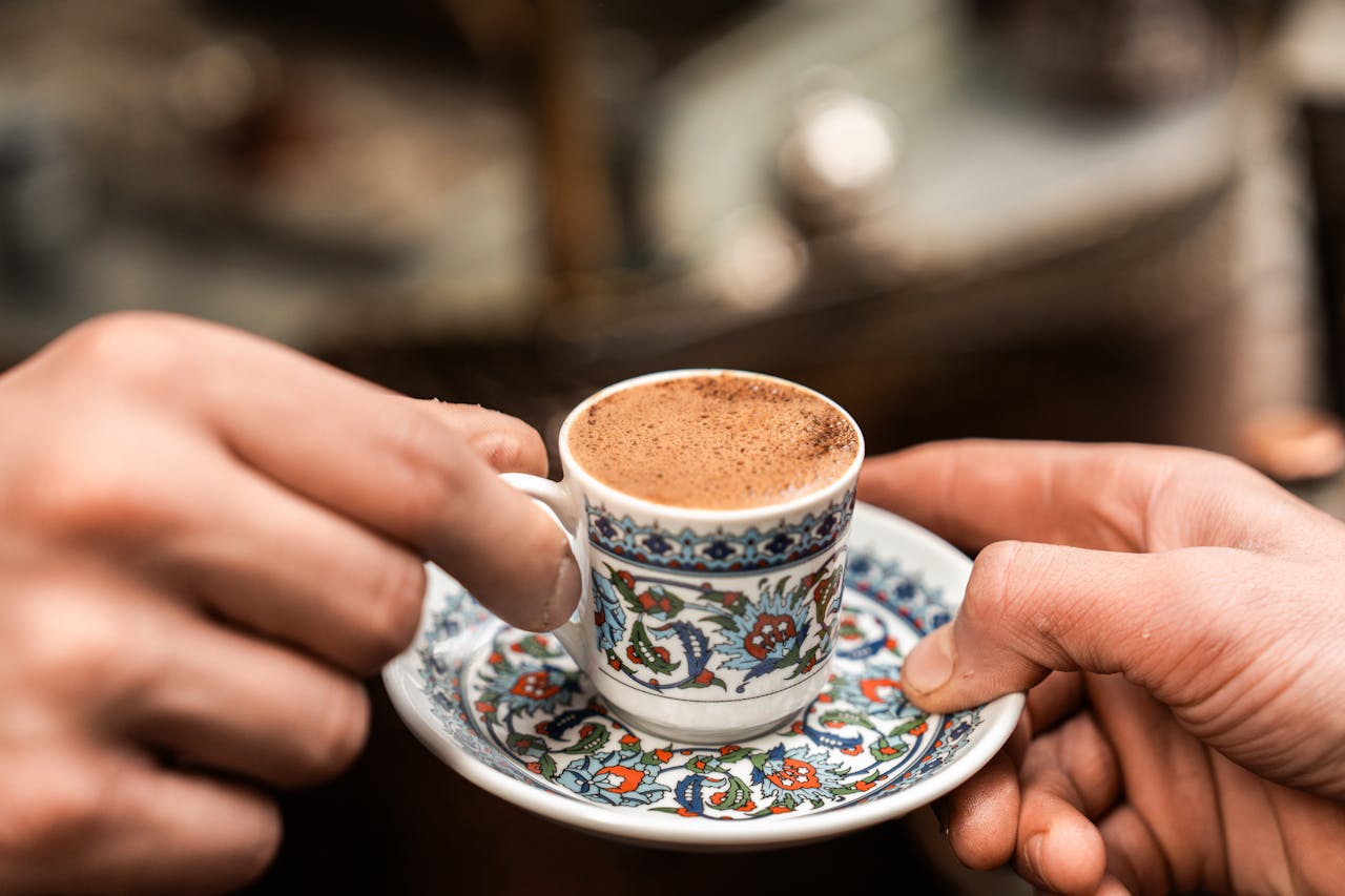 Close-up of Turkish coffee in a floral patterned cup being handed over by two people.