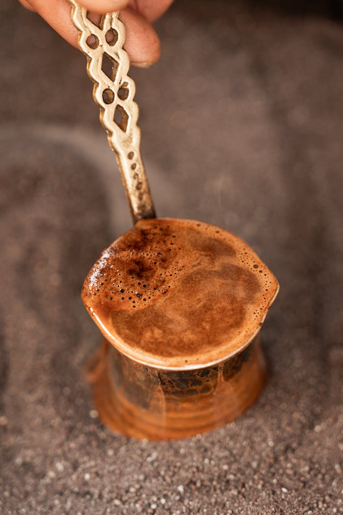 Close-up of Turkish coffee brewing in an ibrik, highlighting rich foam and ornate handle.