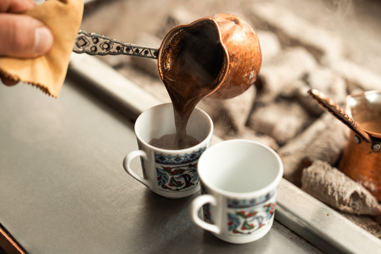 Close-up of hot Turkish coffee being poured into decorative cups with intricate pattern.